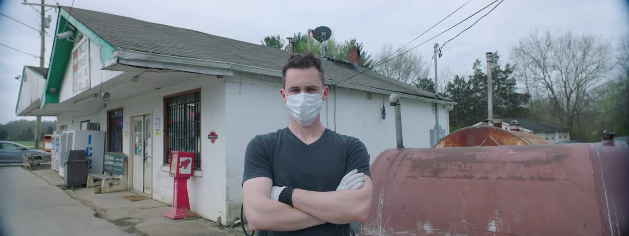 Man wearing a mask due to corona virus stands crossed arms at the gas station