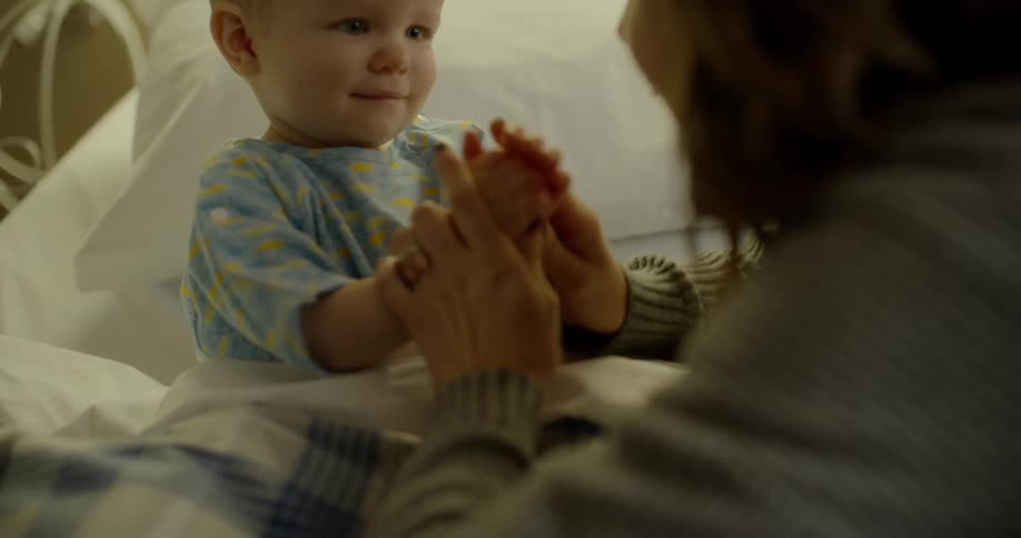 Mother plays with her child who lies in bed
