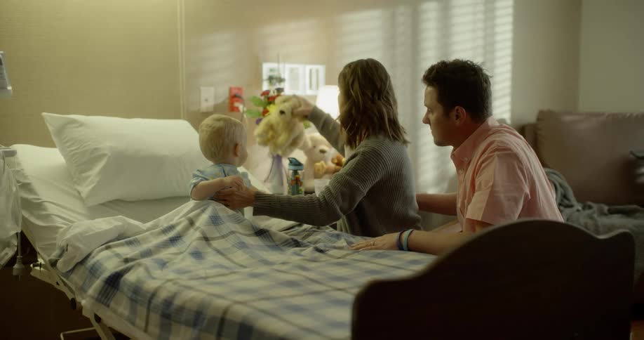 A mother and father comfort their son in a hospital bed