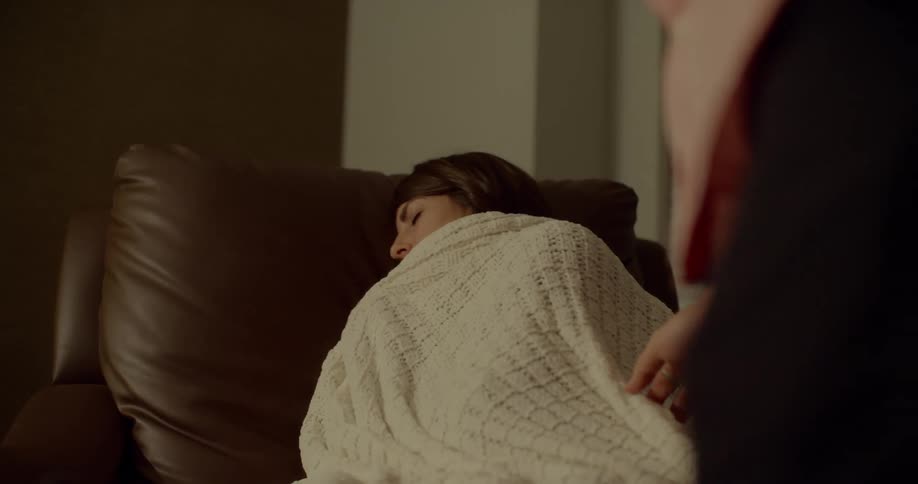 A man tucking in a woman who is sleeping on a couch