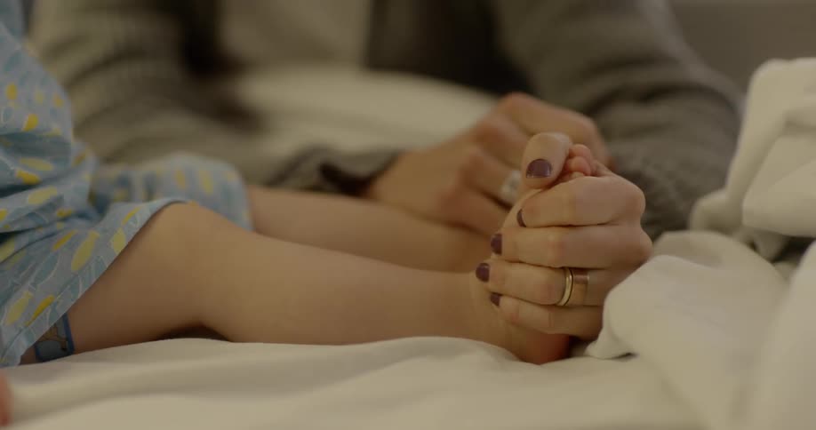 A mother holds her sons food in her hand and squeezes it as they lie in bed