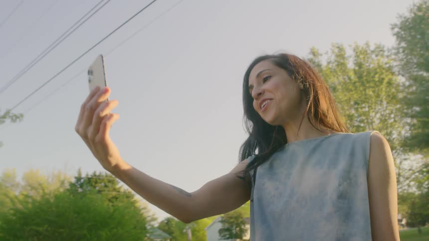 Woman standing on the road makes a video call with a smartphone in the late afternoon