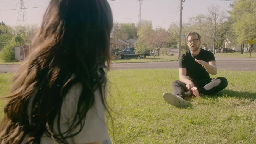 A man and woman sit on the grass and talk while keeping an appropriate social distance between them