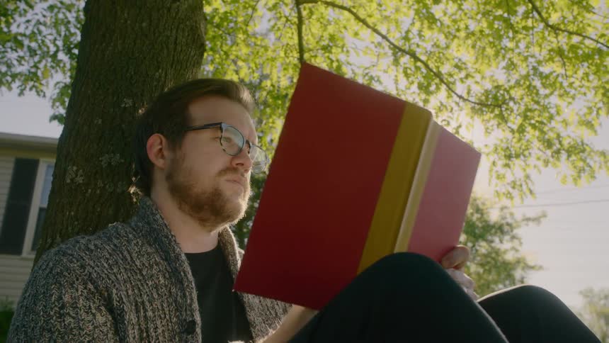 A man reads a book against a tree