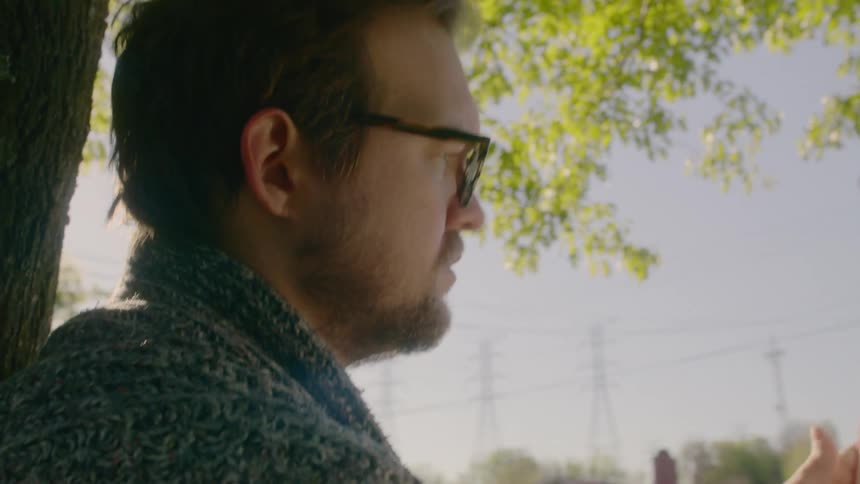A man sitting against a tree reading from a book