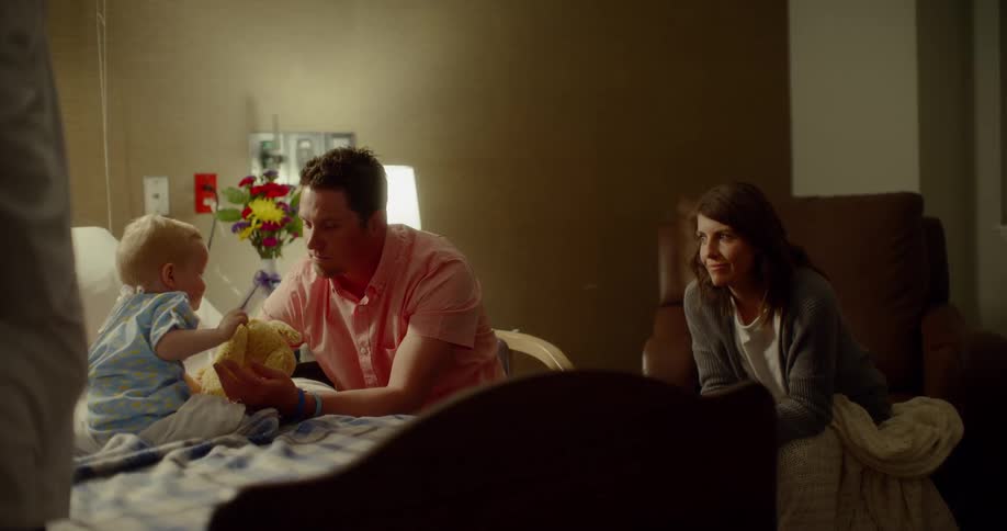 A man plays with his son in a hospital bed while chatting with a doctor