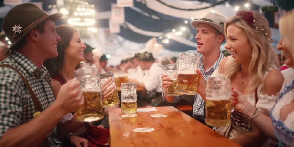 A table full of people hold glasses of beer and laugh and sway