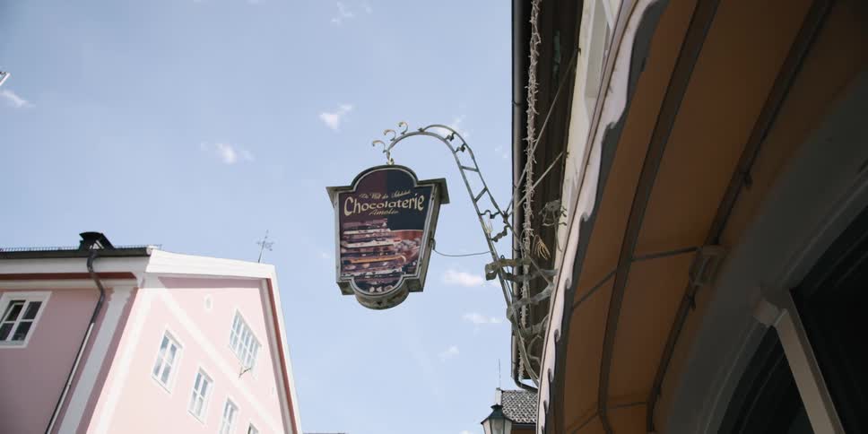 Sign designates a chocolate shop in buildings under a lightly clouded sky