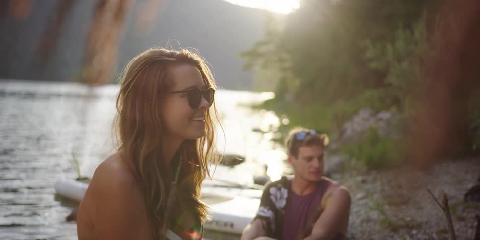 Woman and man sitting by the lake talk to the friends at sunset