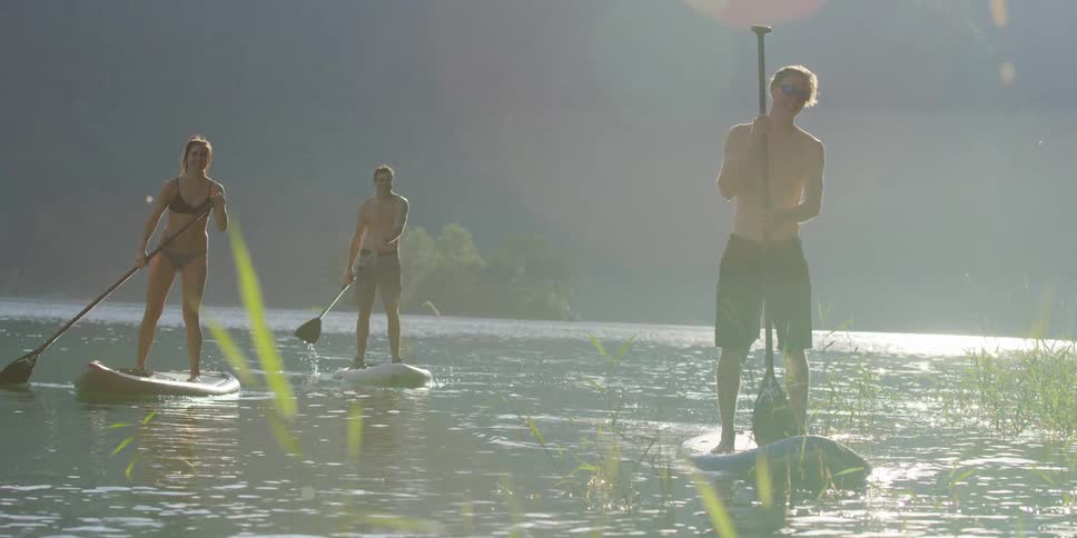 The sun shines and shimmers on the water surface as three friends paddle board