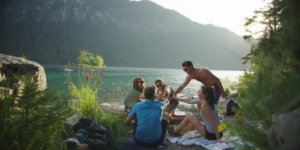 A group of people drink while sitting near a lake