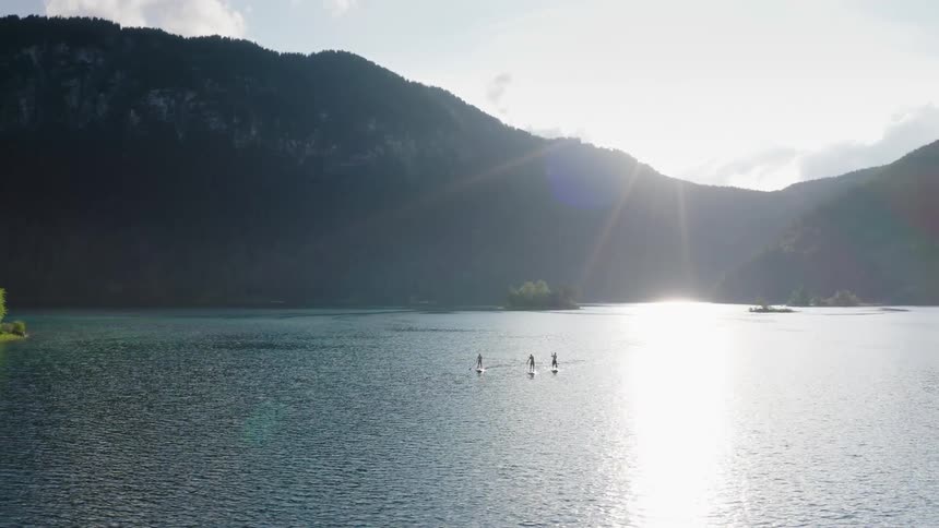 Three people stand on the boards and uses paddles to travel across the lake