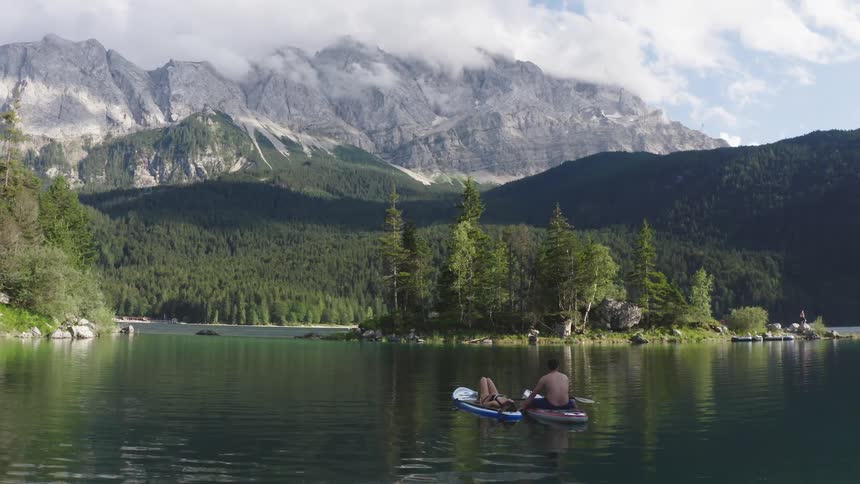 Man and woman sitting on the paddle boards watch the high mountain landscape on the lake