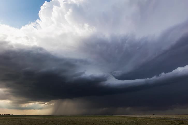 A grassy plain with vehicles driving by with the sky and clouds above