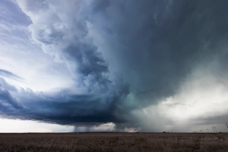 A grassy plain with lightning and storm clouds in the background