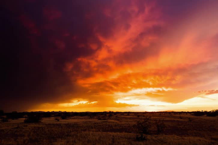 As the sun sets over the desert storm and funnel clouds gather glowing orange and yellow