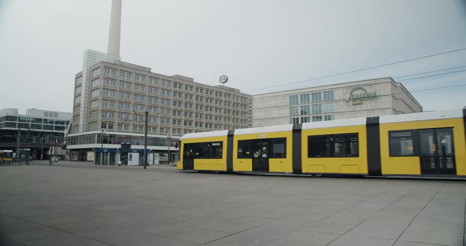 Seemingly empty light rail train passes by building under cloudy sky