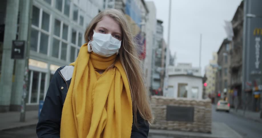 Blonde woman wearing mask and scarf stands in middle of street