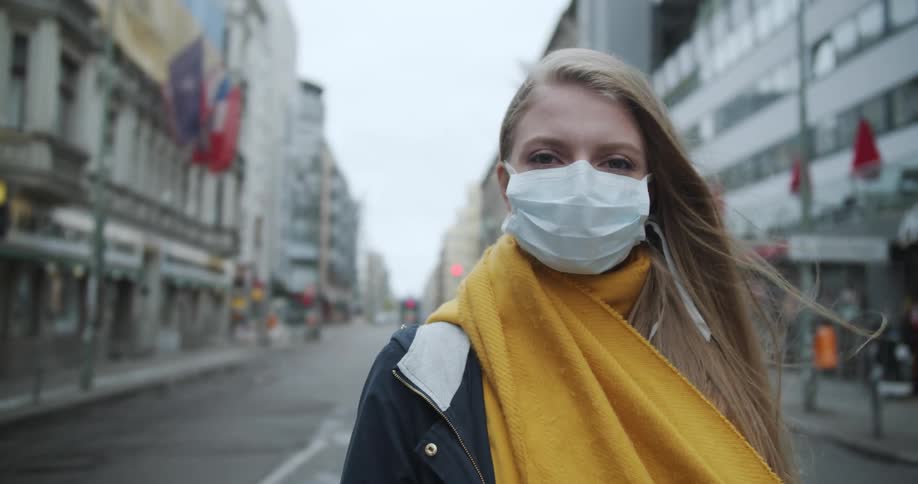 A teenager wearing a mask stands in an empty city street