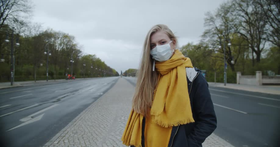 A woman stands on an empty highway median wearing a medical face mask