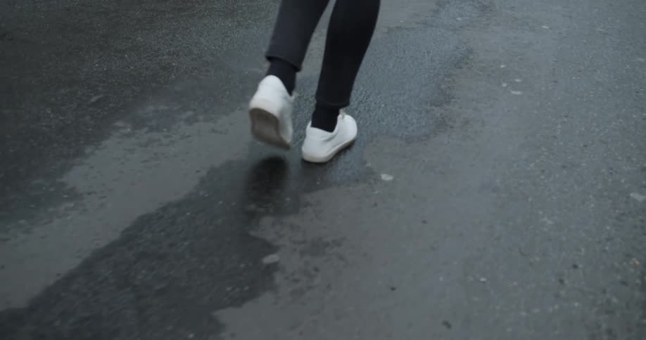 A person wearing black skinny jeans and white sneakers walks on a rain wet road