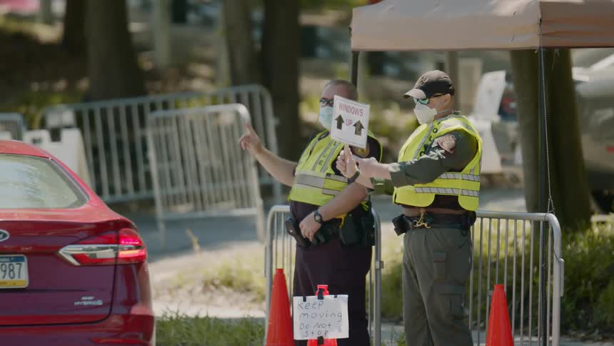 Two policemen stand on a street and give instructions to motorists