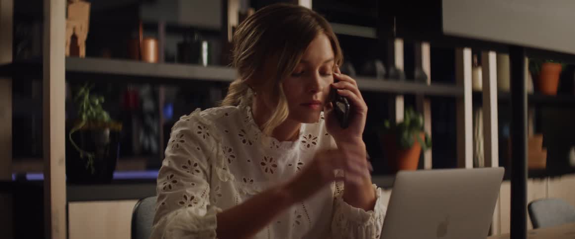 A woman looks at her laptop and talks on the phone and then looks as if she heard some bad news