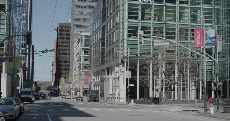 People wearing masks cross a nearly empty city street on a sunny day