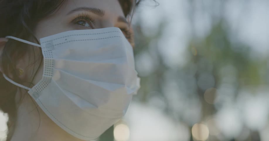 Woman wearing mask stands outdoors looking around