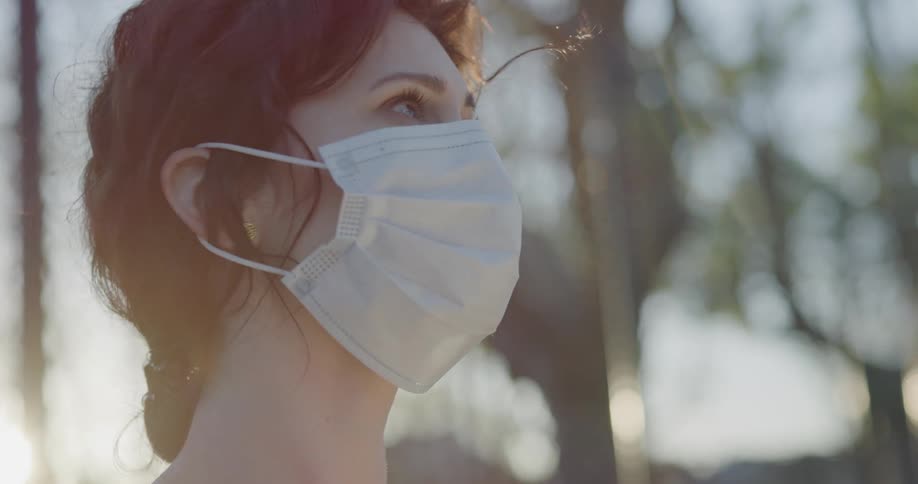 A woman looks around outside while wearing a mask