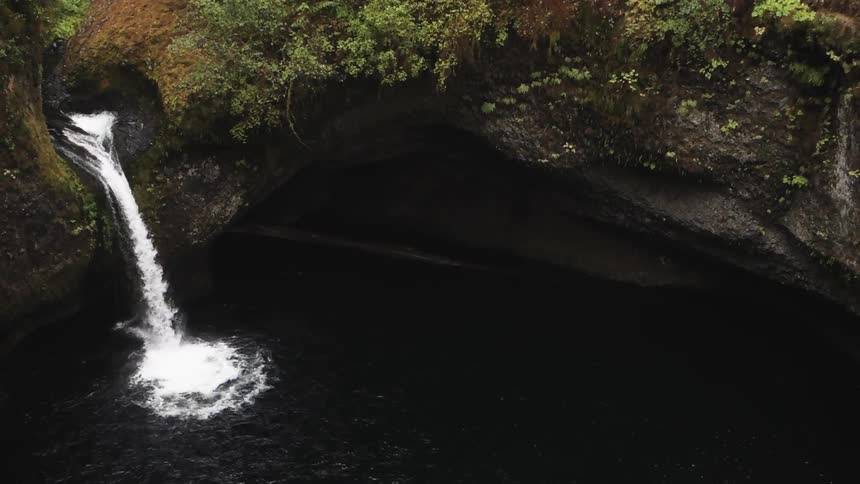 A waterfall pours over a ledge and into a dark pool of water