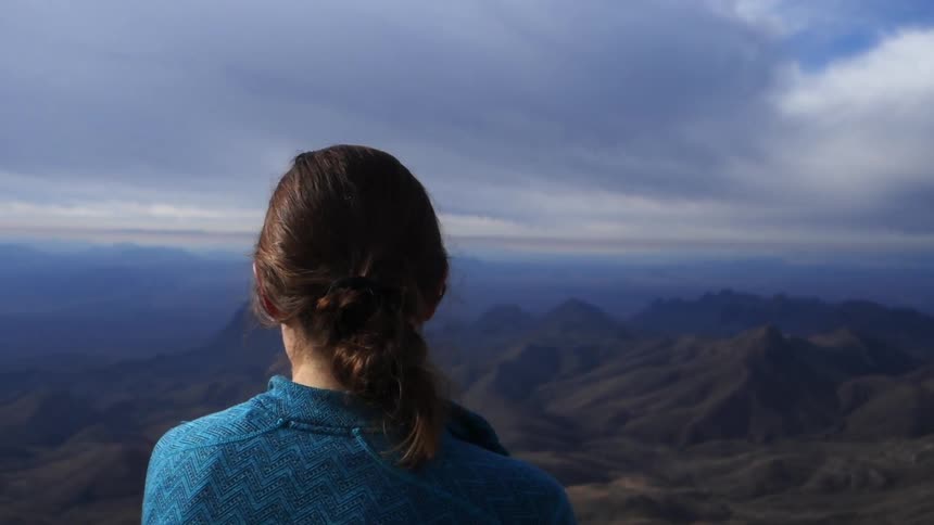 A woman stands overlooking a mountain range on a cloudy day