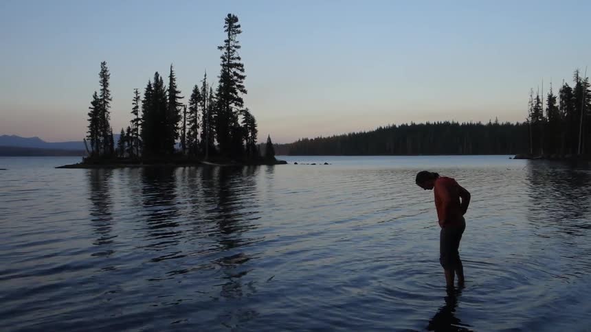 A man wades in a rippling lake at dusk