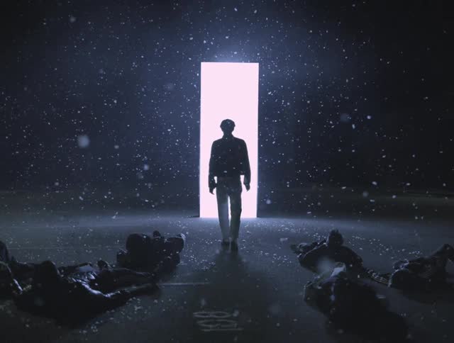 A man walks toward a panel of light and others get up from the ground in a choreographed manner