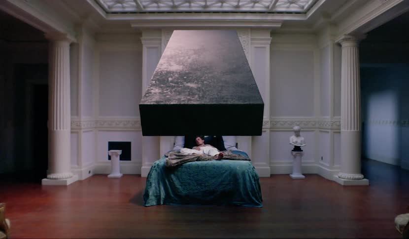 A man sleeping in a bed as a black monolith floats over him
