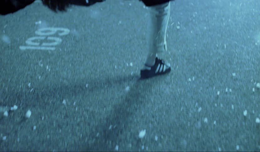 White fluff swirls around a man who is suspended bent backward with just one leg on the ground in a parking lot at night