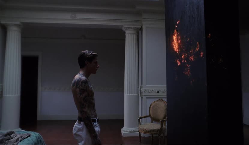 Shirtless tattooed man walks up to mystic stele in the living room of a luxurious house