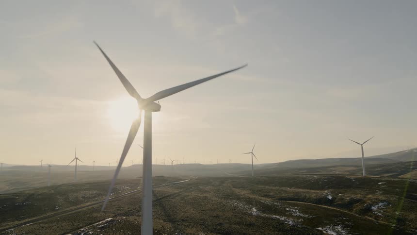 Medium close up orbit of a wind turbine in the foreground of a wind farm on hilly countryside