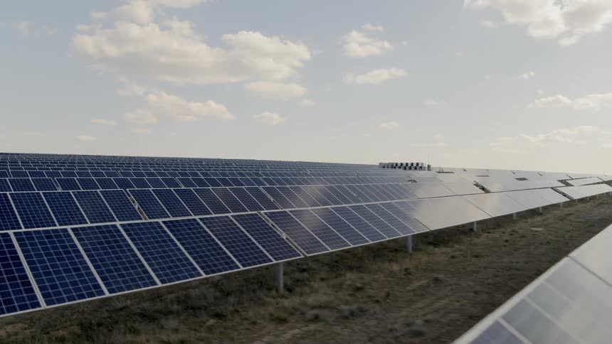 Low traverse over solar panels with blue sky and beautiful clouds reflecting on their surface