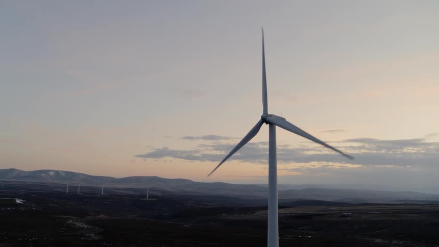 A wind turbine operates under a painted sunset sky