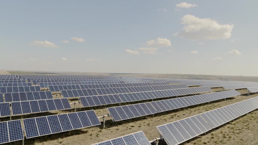 Flying over rows of solar panels under blue skies and puffy clouds