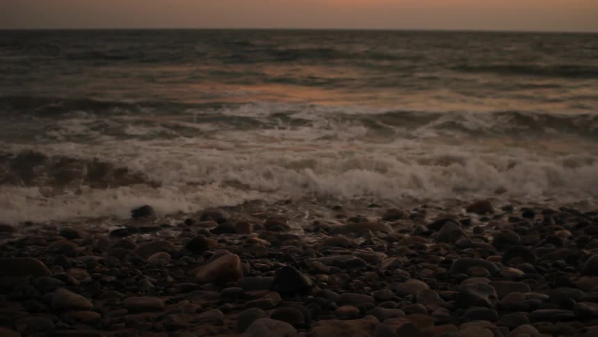 Water is crashing on the shore at sunset