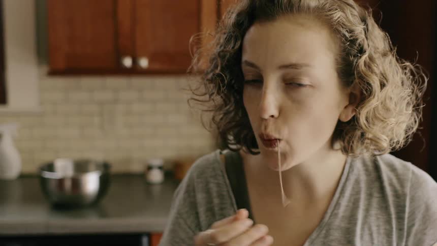 A woman eats a piece of spaghetti