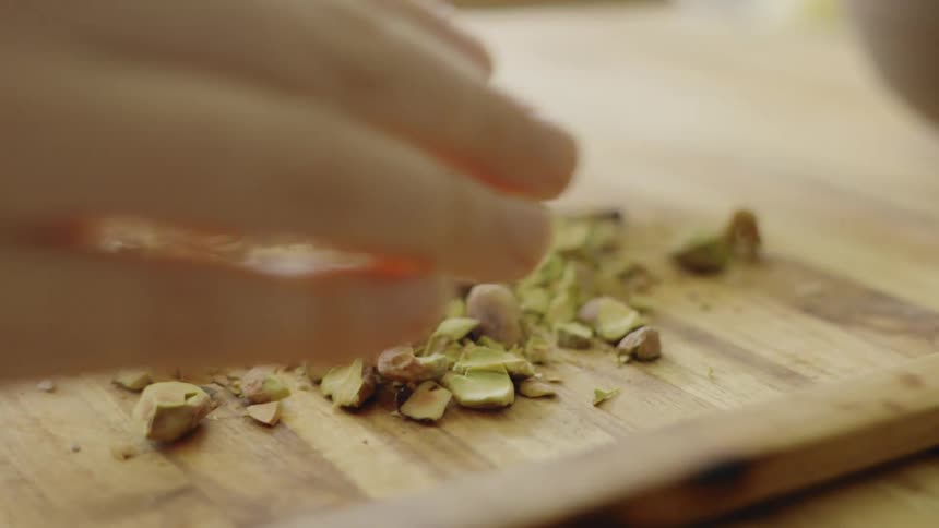 A person uses a knife to chop garlic on a wooden cutting board