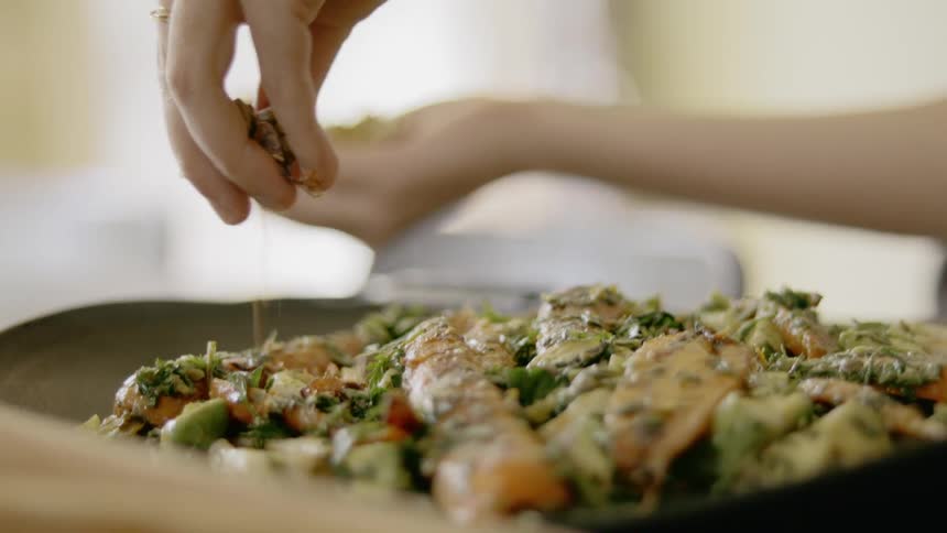 A woman sprinkles garnish on a meal in a bowl
