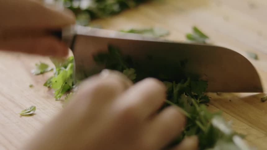 Person uses knife to chop herbs on kitchen board