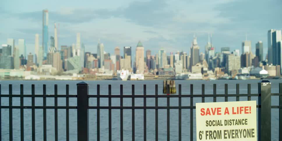 Sign advising social distancing hangs on fence across water from downtown