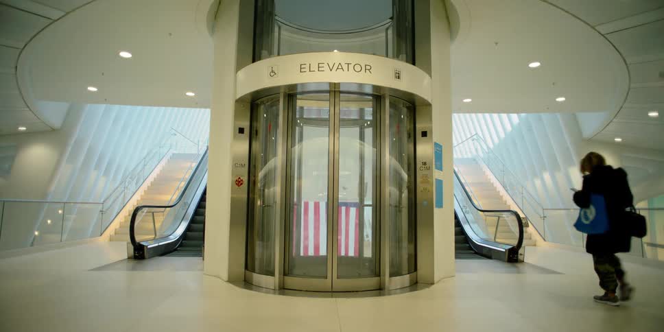 A circular glass elevator flanked by escalators in an elaborate building