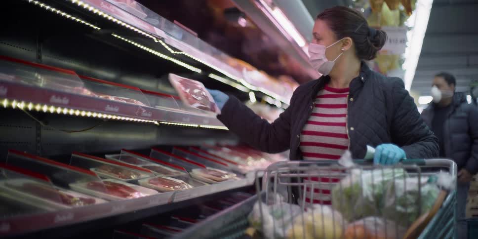 Woman wearing medical face mask shopping in meat aisle at grocery store