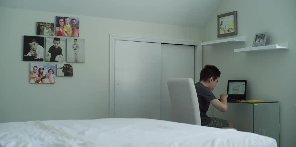 A boy sits at a desk and looks at his laptop